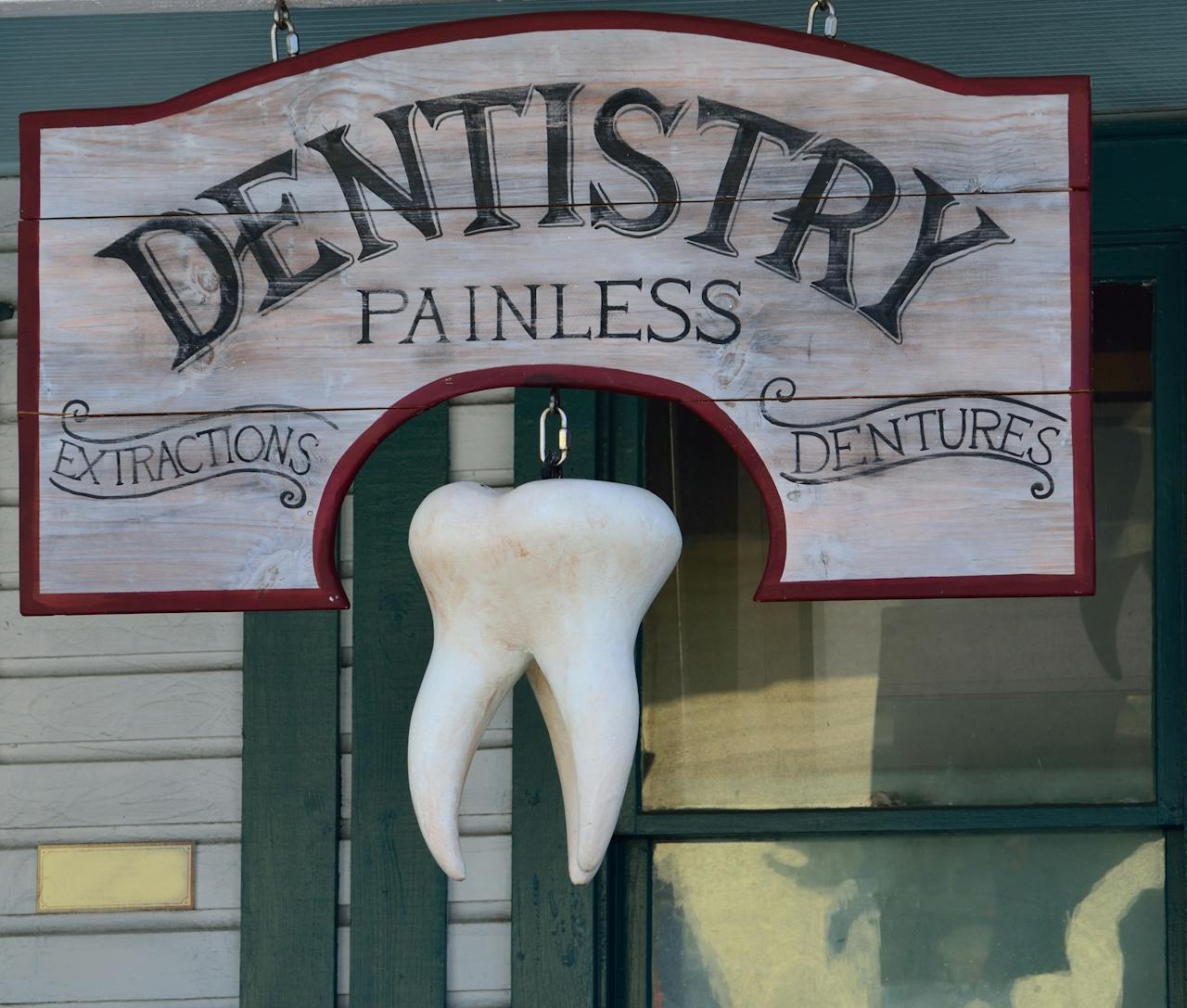 Classic dental sign with a hanging tooth, advertising painless extractions and dentures.